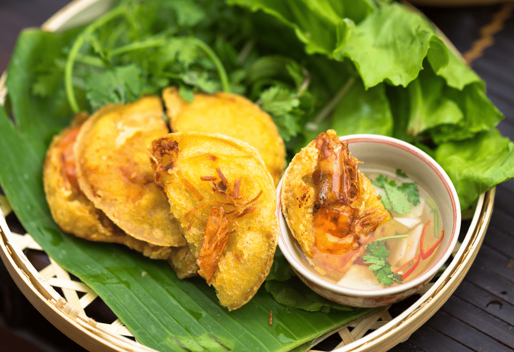 Banh tom Ho Tay is made with whole freshwater shrimp and sweet potato, deep-fried to golden perfection and served with fresh herbs (Source: Canva)